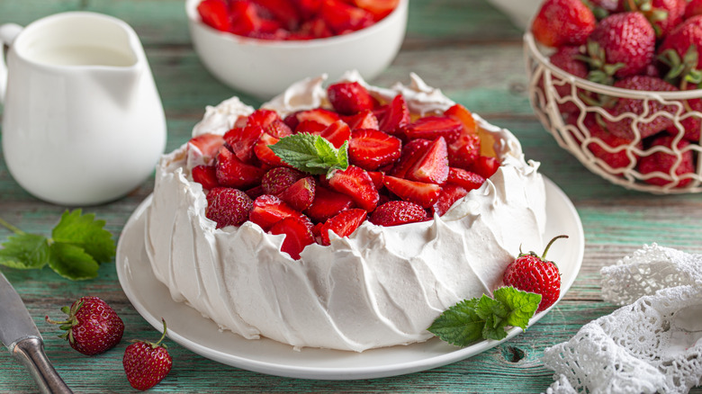 A pavlova cake with strawberries sits on a table.