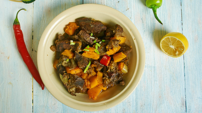 A bowl of Guyanese pepperpot stew sits on a painted wooden table.