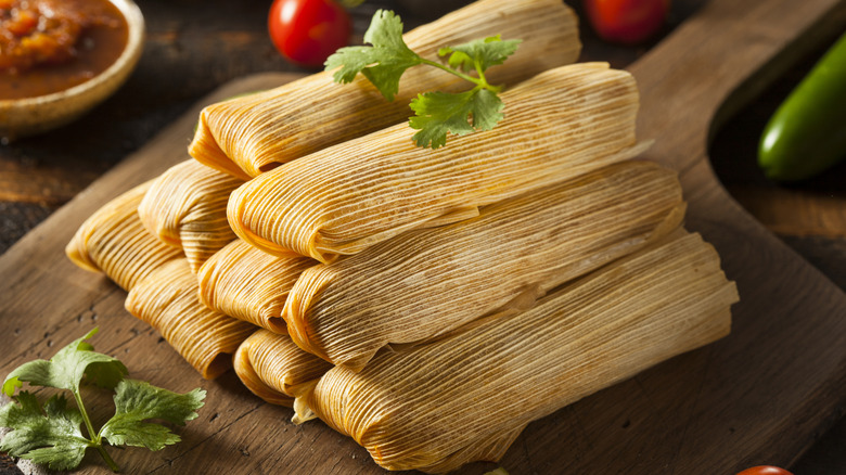 Homemade tamales wrapped in corn husks sit on a table.