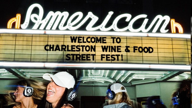 A sign for the Charleston Wine & Food Street Fest with women dancing wearing headphones