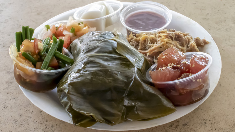 A white styrofoam plate with Hawaiian food, including poke, salad, pulled pork, and poi