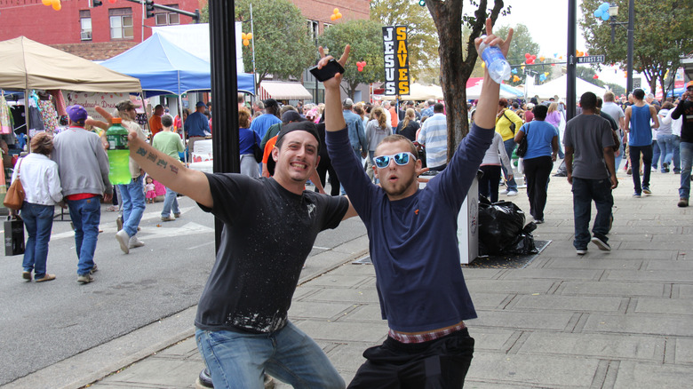 Two men smile and pose for the camera on the sidewalk at the Lexington Barbecue Festival