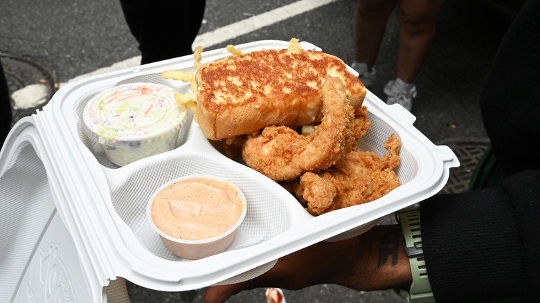 A white takeout tray of fried chicken with toast, fries, coleslaw, and sauce