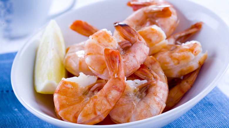 Cooked shrimp in a white bowl with a lemon slice on top of a blue napkin