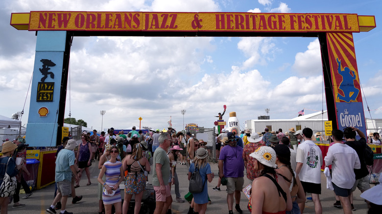 Crowds at the New Orleans Jazz & Heritage Festival walk underneath a large sign