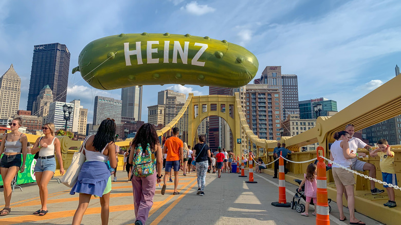 People walking on a bridge at the Picklesburgh festival with a giant Heinz pickle balloon overhead