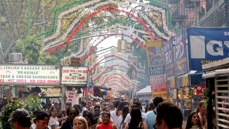 Crowds at the Feast of San Gennaro with green, white, and red decorations over the street