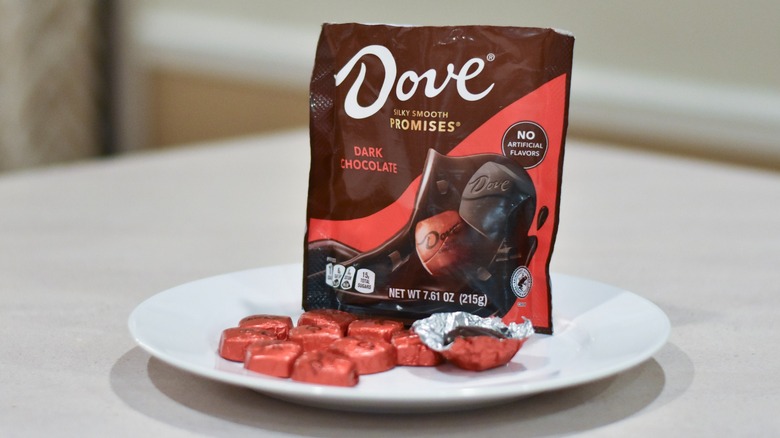 A bag of Dove promises dark chocolates next to individual chocolates on a white plate