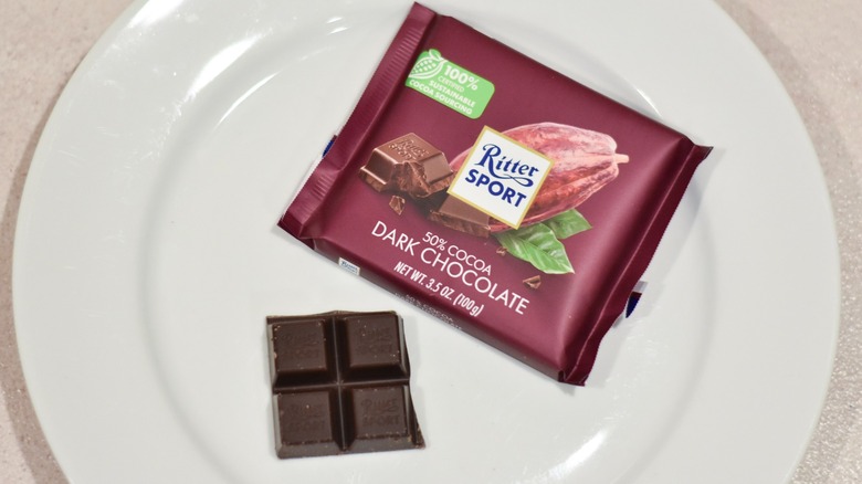 A square of Ritter dark chocolate next to the candy bar wrapper on a white plate