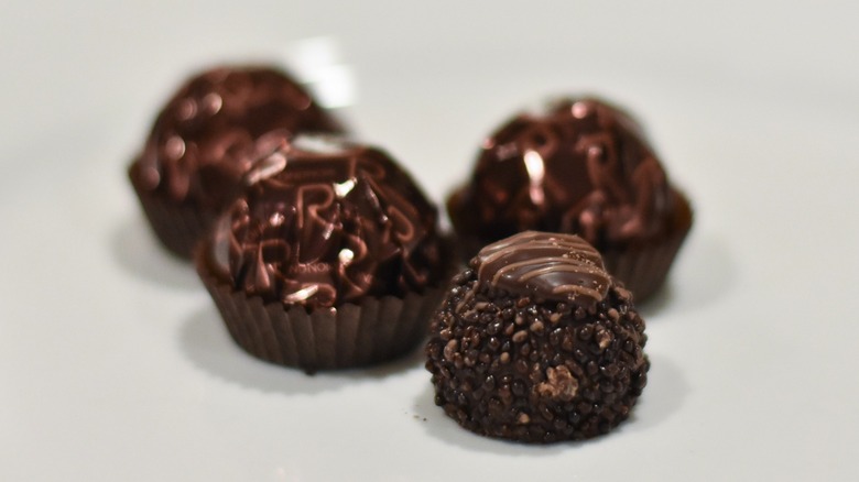 An unwrapped Ferrero dark chocolate next to wrapped versions on a white plate