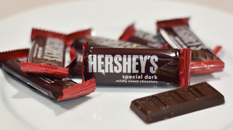 A stack of Hershey's special dark chocolate packages next to a bar of chocolate on a white plate