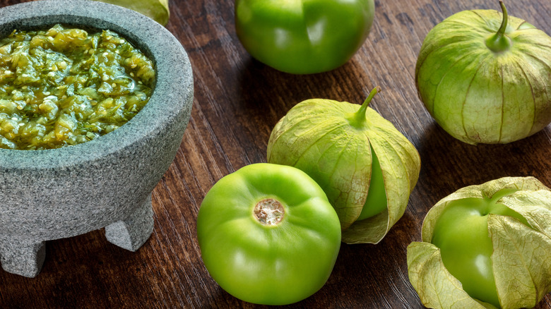 Fresh tomatillos next to a bowl of salsa verde