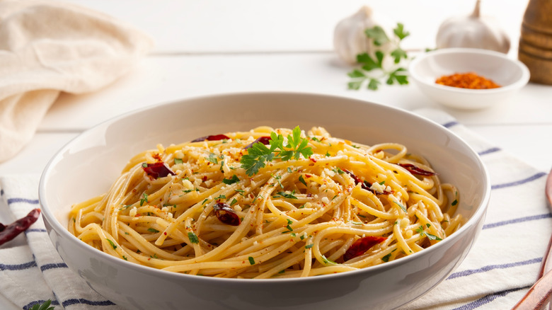 Spaghetti aglio e olio in a bowl with fresh garlic bulbs and red pepper flakes in the background