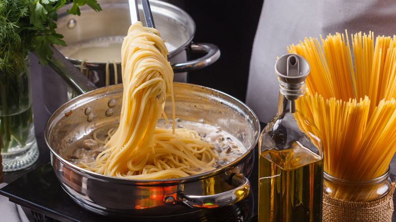 Spaghetti prepared in a pan with starchy pasta water in background