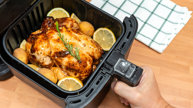 Hand pulls out an air fryer basket full of lemon slices, potatoes, and a roasted chicken