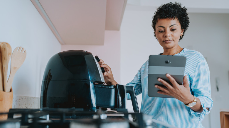 A woman holding a tablet and learning how to use an air fryer