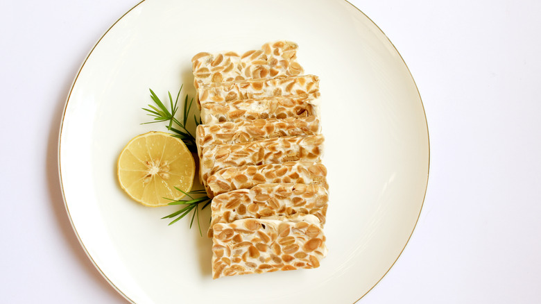 Sliced tempeh in a plate with a lemon and herbs