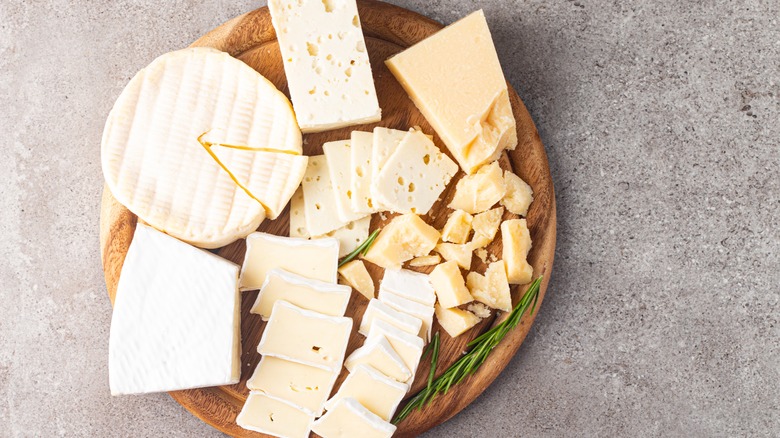 Wooden board with various cheese and olives. Cheeses include brie, Camembert, Parmesan, feta, and blue cheese.