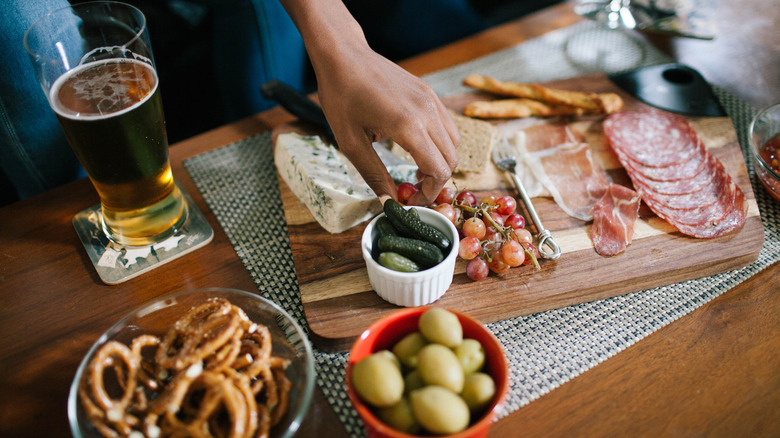 Hand reaches for grapes on a charcuterie board containing meat, cheese, pickles, grapes, and crackers