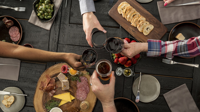 Overhead view of friends toasting over a table with various plates and bowls of charcuterie items