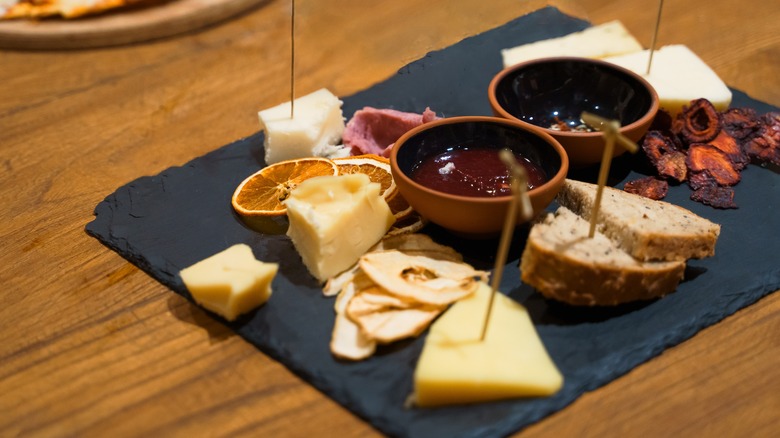 Charcuterie board with cheeses, bread, dried fruits, and bowls of spread