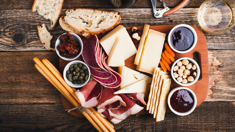 Charcuterie board on a table with meats, cheeses, bread, crackers, spreads, and nuts