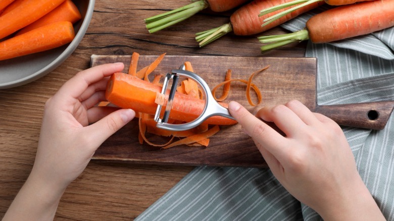 Person peeling carrot on board