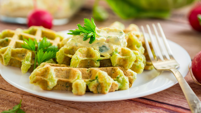 a waffle cooked with herbs sits on a plate with a fork