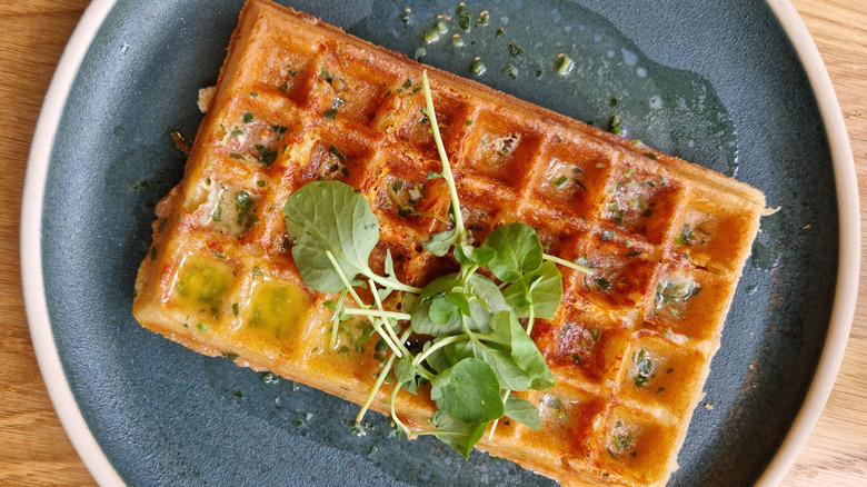 a savory waffle with herbs sits on a dark plate