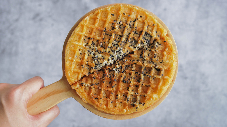 hand holding sesame scallion waffles on wood serving board