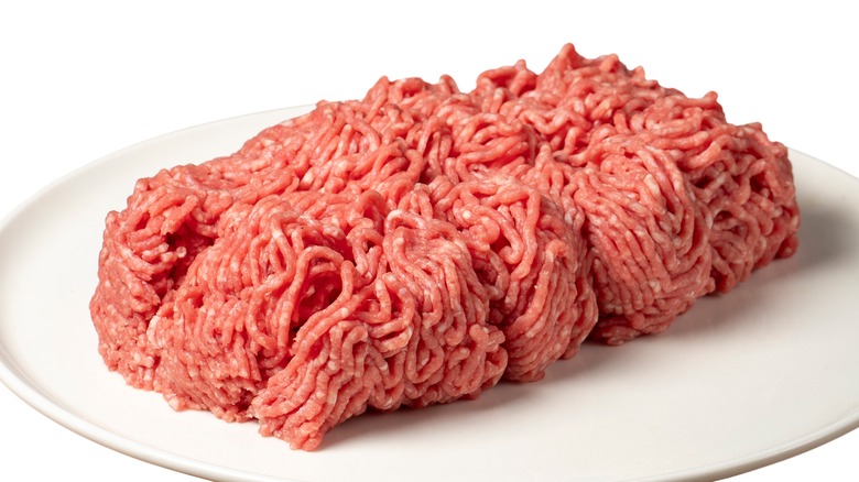 A white plate of raw ground beef displayed on a white background