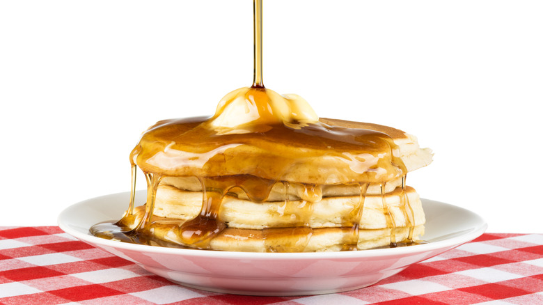 pouring syrup on stack of pancakes