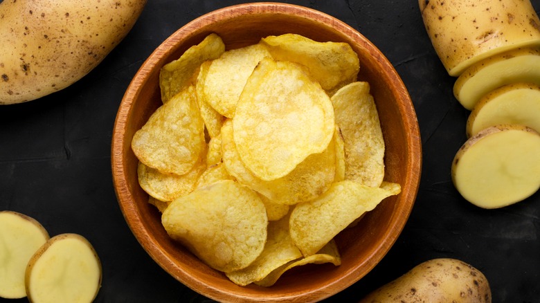 wooden bowl of potato chips surrounded by fresh potatoes