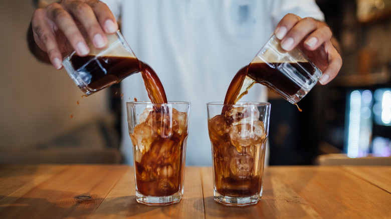 Hands pour cold brew into glasses