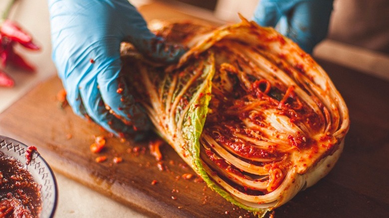 Gloved hands spreading red paste on napa cabbage