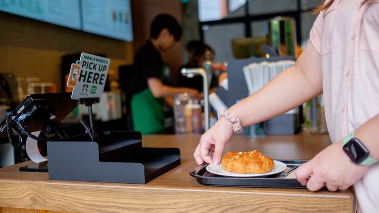 Person picking up a croissant on a plate inside Starbucks