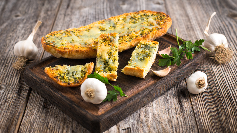 garlic bread on a wooden board with whole garlic bulbs on the side