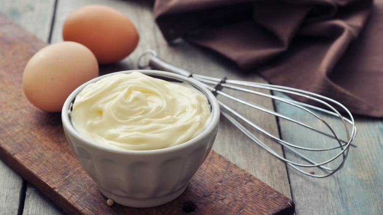 Bowl of mayonnaise with whisk and eggs