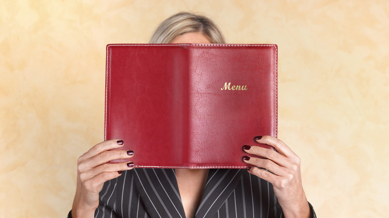 A woman holding a menu in front of her face.
