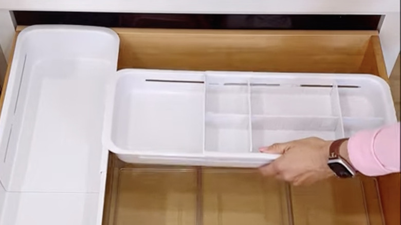 A hand placing floating bins in a deep kitchen drawer.