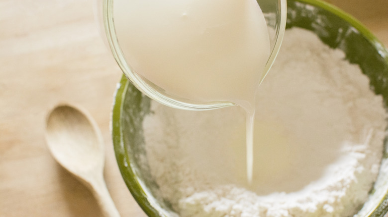 pouring buttermilk into a bowl of flour