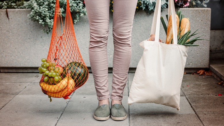 Girl holds two grocery bags, one with produce and one with bread