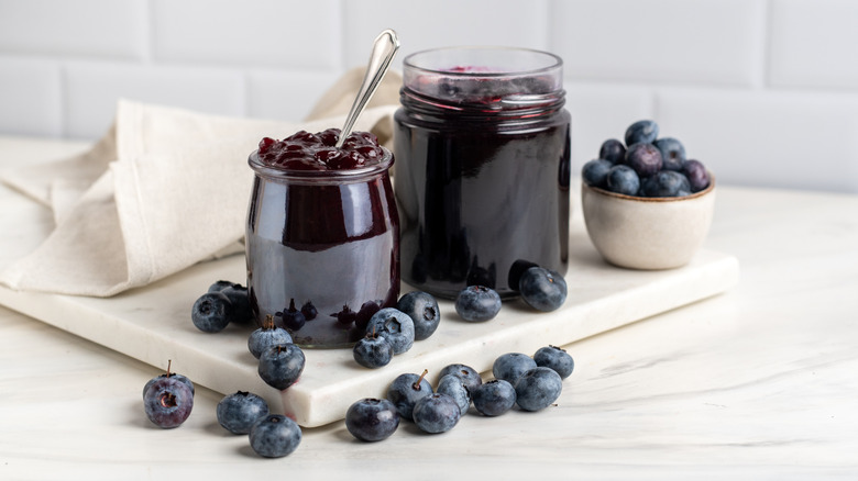 Blueberry pie filling in clear glass jars on a white cutting board.