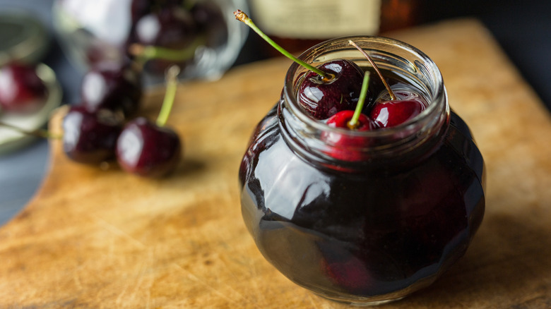 A jar of bourbon-soaked cherries sits on a cutting board.