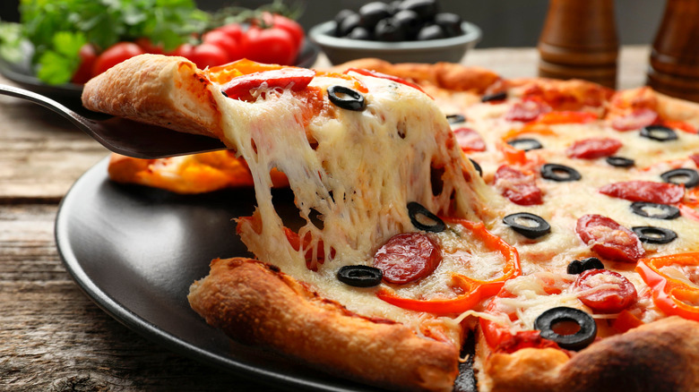 person lifting a slice of cheesy pizza from a whole pizza pie