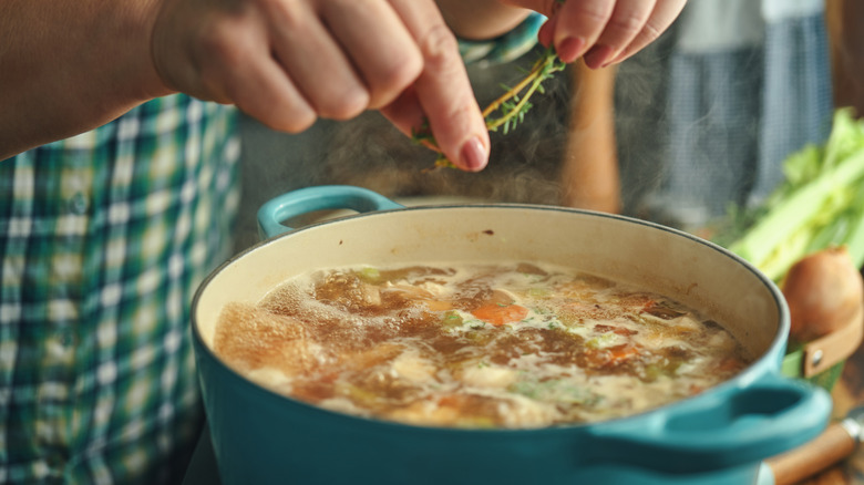 person adding herbs to pot of chicken stock