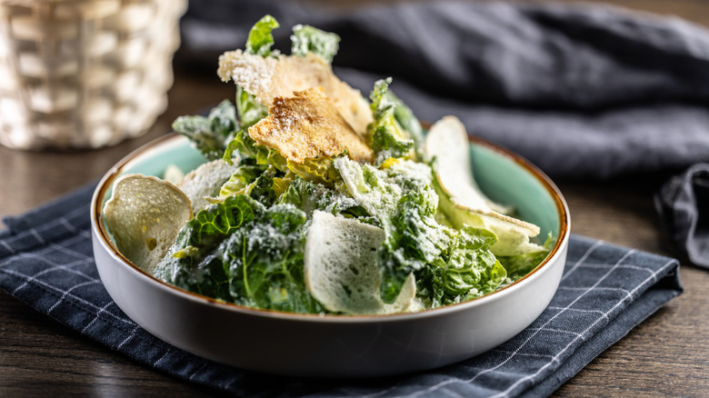 a Caesar salad sits in a bowl against a rustic background