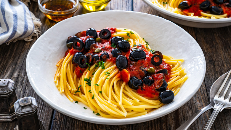 A bowl of spaghetti puttanesca sits on a wooden table