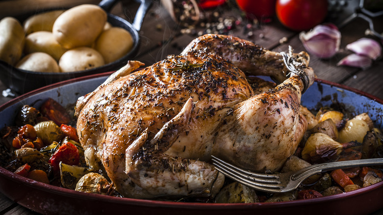 a whole chicken sits in a blue pan surrounded by vegetables