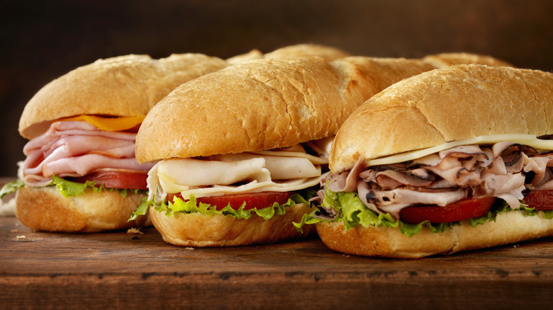 three deli meat sandwiches on wooden cutting board